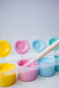 Colorful paint pots with brush in pastel shades.