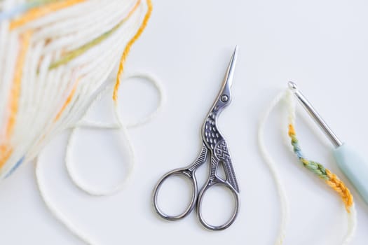 Crochet tools and yarn ball with bird shaped scissors on white surface.