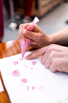Hand decorating with pink icing on paper using piping bag.