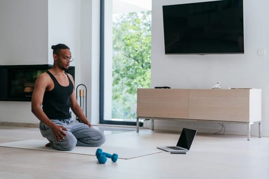 Training At Home. Sporty African American man doing the training while watching an online tutorial on a laptop, exercising in the living room, free space.