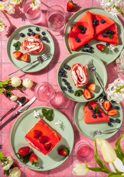 Pink colored crepes and rolled strawberry cake served on green plates with fresh fruit, accompanied by glasses and cutlery, perfect for a spring brunch