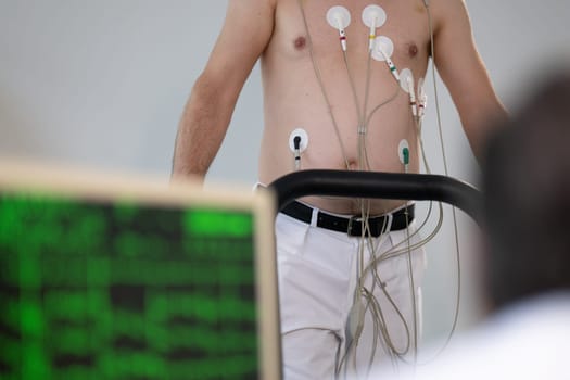 A middle-aged man is undergoing a medical stress test on a treadmill, connected to ECG electrodes for heart monitoring in a clinical environment.