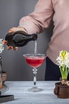 Bartender pouring sparkling wine into a cocktail glass with red liquor, ice, and flower decorations for a refreshing drink