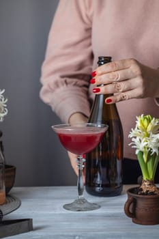 Bartender placing a bottle of sparkling wine near a red cocktail in a coupe glass, ready to be topped up