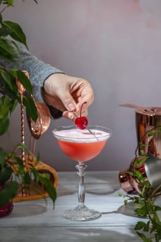 Bartender is garnishing a vibrant pink cocktail in an elegant glass with a fresh cherry, adding a final touch to the refreshing drink