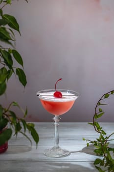 Vibrant pink cocktail, topped with a creamy foam and a bright red cherry, sits in a classic stemmed glass, promising a delightful taste experience