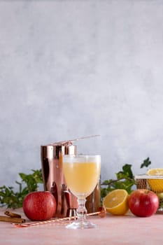 Refreshing apple cocktail served in a glass, garnished with cinnamon sticks and lemon slices, alongside a cocktail shaker and fresh apples