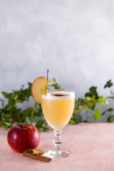 Apple cider cocktail in elegant glass, garnished with fresh apple slice and cinnamon sticks, embodies autumnal flavors