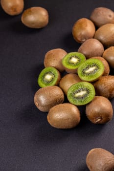 Kiwi fruits, whole and halved, create a vibrant display on a dark surface, emphasizing their freshness and texture