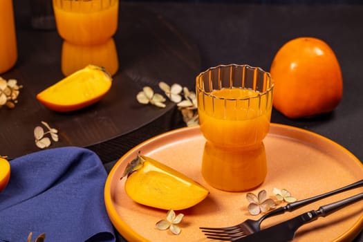 Glass of vibrant persimmon juice accompanied by fresh persimmon slices on a stylish plate, creating a sophisticated table setting