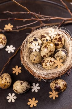 Small speckled quail eggs resting in a cozy nest, adorned with delicate felt flowers and bare branches, evoke a sense of spring and new beginnings