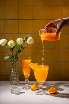 Bartender pours fresh orange juice from a decorative bottle into a crystal glass, creating a refreshing drink, garnished with an orange slice