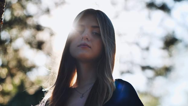 Backlit portrait of a young woman enjoying sunlight in nature, with lens flare adding a dreamy atmosphere