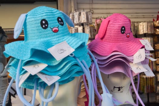 Crete.Greece - april 02, 2025: Playful hats with floppy ears and smiling designs stacked on mannequin heads, combining bright blue and pink shades for a cheerful display in a shop.