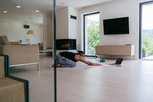 Training At Home. Sporty African American man doing the training while watching an online tutorial on a laptop, exercising in the living room, free space.