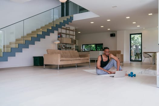 Training At Home. Sporty African American man doing the training while watching an online tutorial on a laptop, exercising in the living room, free space.