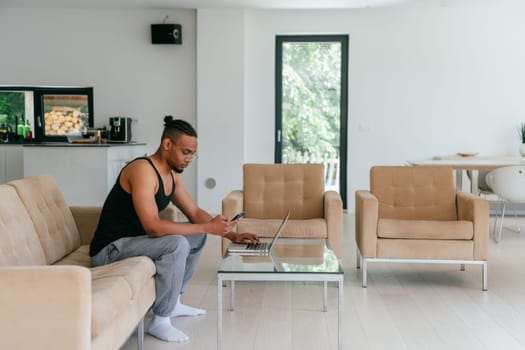 African American man in glasses sitting at a table in a modern living room, using a laptop for business video chat, conversation with friends and entertainment.