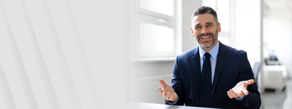 A middle aged businessman in a suit holds a discussion in a well-lit office. He appears confident and approachable, showcasing a successful and professional lifestyle in a contemporary environment.