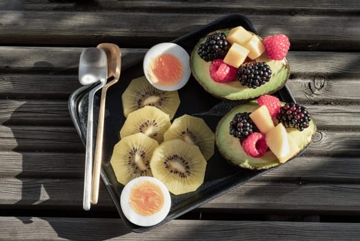 Top view of vibrant healthy food with blackberry, redberry and mango on avocado with golden kiwi and boiled egg is eating colorful on ceramic dish. Breakfast plate with fruits, use it as your space for text, design, wallpaper and poster.