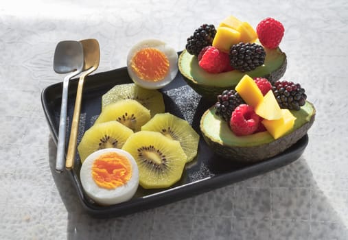 A colorful healthy food with redberry, blackberry and mango on avocado with golden kiwi and boiled egg on vibrant eating ceramic dish. Breakfast plate with fruits, use it as your wallpaper, poster and copy space.