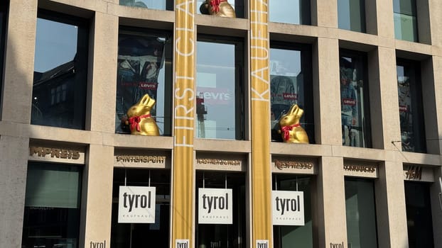 28.03.2025 Austria: Shopping Center Kaufhaus Tyrol Easter Decorations with Lindt Golden Bunnies. Easter decorations at Kaufhaus Tyrol shopping center in Innsbruck, Austria. The modern building facade is adorned with large golden Lindt chocolate bunnies with red ribbons, creating a festive holiday atmosphere. The golden banners complement the seasonal decor, enhancing the celebratory spirit of springtime in the city.