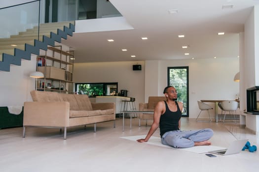 Training At Home. Sporty African American man doing the training while watching an online tutorial on a laptop, exercising in the living room, free space.