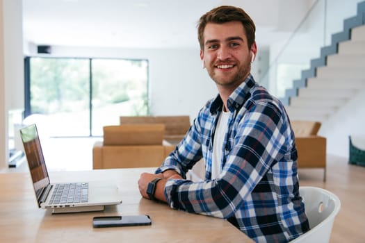 A freelancer sitting at a table in a modern living room, with headphones using a laptop for business video chat, conversation with friends and entertainment.