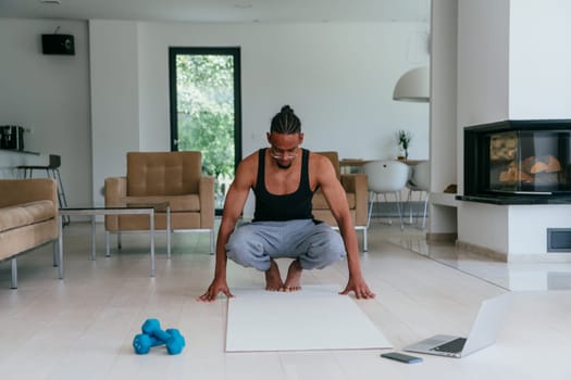 Training At Home. Sporty African American man doing the training while watching an online tutorial on a laptop, exercising in the living room, free space.
