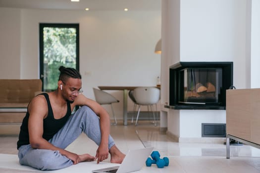 Training At Home. Sporty African American man doing the training while watching an online tutorial on a laptop, exercising in the living room, free space.