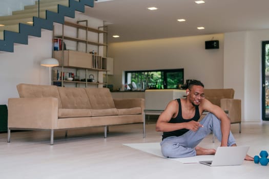 Training At Home. Sporty man doing the training while watching an online tutorial on a laptop, exercising in the living room, free space