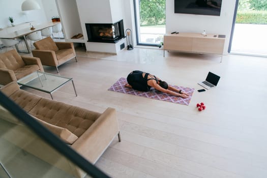 Young Beautiful Female Exercising, Stretching and Practising Yoga with Trainer via Video Call Conference in Bright Sunny House. Healthy Lifestyle, Wellbeing and Mindfulness Concept.