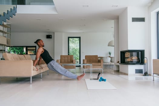 Training At Home. Sporty man doing the training while watching an online tutorial on a laptop, exercising in the living room, free space