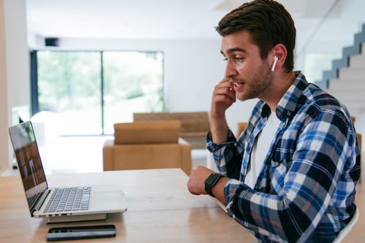 A freelancer sitting at a table in a modern living room, with headphones using a laptop for business video chat, conversation with friends and entertainment.