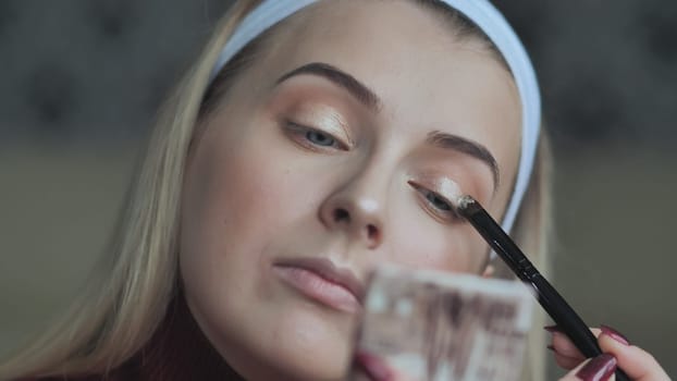 A blonde girl applies makeup to her eyelids