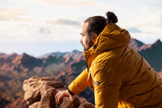 Male hiker looks out over a breathtaking mountain range from the hill top, embracing the solitude and fresh air of the great outdoors. Sense of adventure and endless nature exploration.