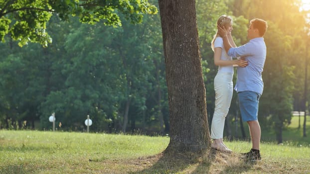 A young man and woman are standing under a tree in a park and hugging