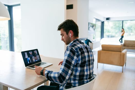 A freelancer sitting at a table in a modern living room, with headphones using a laptop for business video chat, conversation with friends and entertainment.