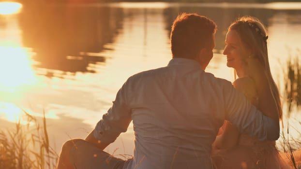 A young couple sits on a lake at sunset