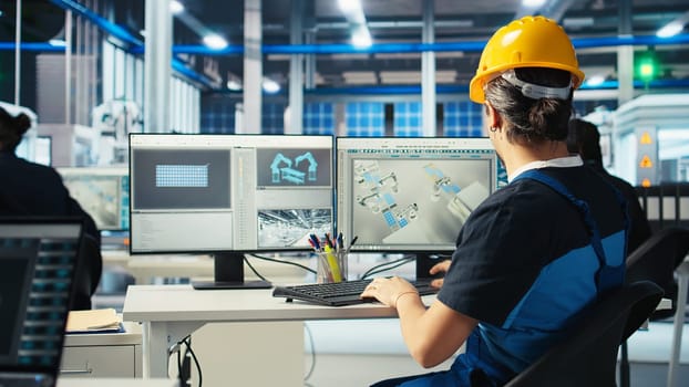 Photovoltaics factory engineer wearing hardhat planning work on facility floor in CAD application. Eco friendly solar panels plant technician designing production lines on PC, camera A
