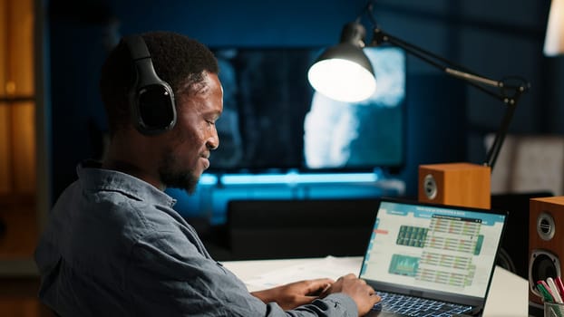 African american analyst works on accounting analysis while he is dancing, feeling the rhythm and checks financial balance. Remote worker listening to favorite groovy music on headphones. Camera B.