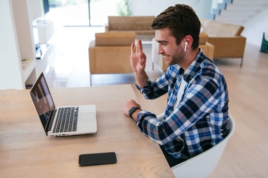 A freelancer sitting at a table in a modern living room, with headphones using a laptop for business video chat, conversation with friends and entertainment.