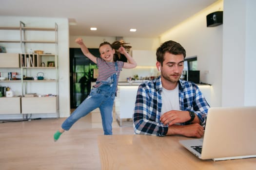 Work from home. Daughter interrupting her father while he is having a business online conversation on his laptop while sitting in the modern living room