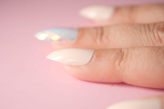 Intricate nail art showcases white and shimmering colors on fingers.