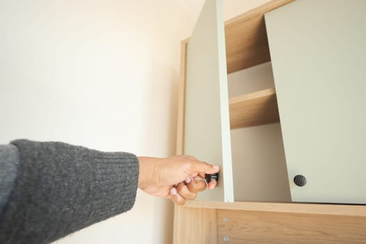 A person reaches for a cabinet door in a bright room.