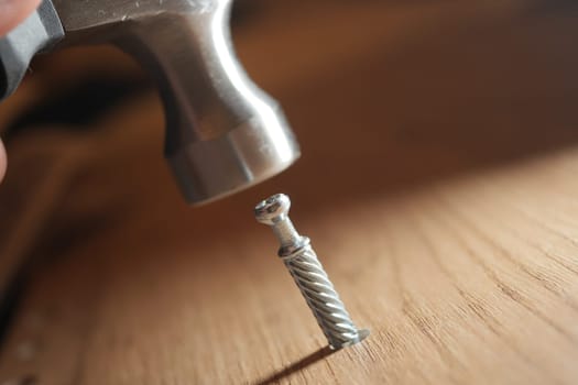 A hammer approaches a screw being installed in wood, showcasing craftsmanship.