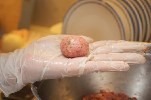 A chef forms a meatball using seasoned ground meat in a bustling kitchen.