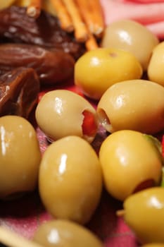 Green olives filled with red pimentos alongside dried fruits on a plate.