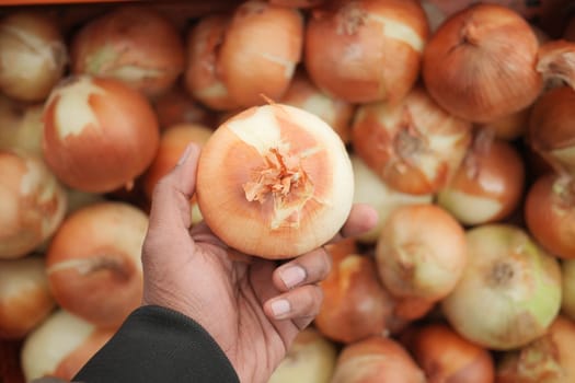 Close-up of a hand grasping an onion surrounded by many others at a market.