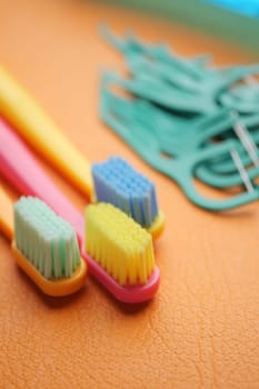 Colorful toothbrushes sit on an orange surface with dental tools nearby.