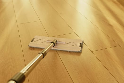 A person is mopping a wooden floor on a sunny afternoon.